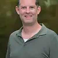 a man in olive green t-shirt smiles for a photo