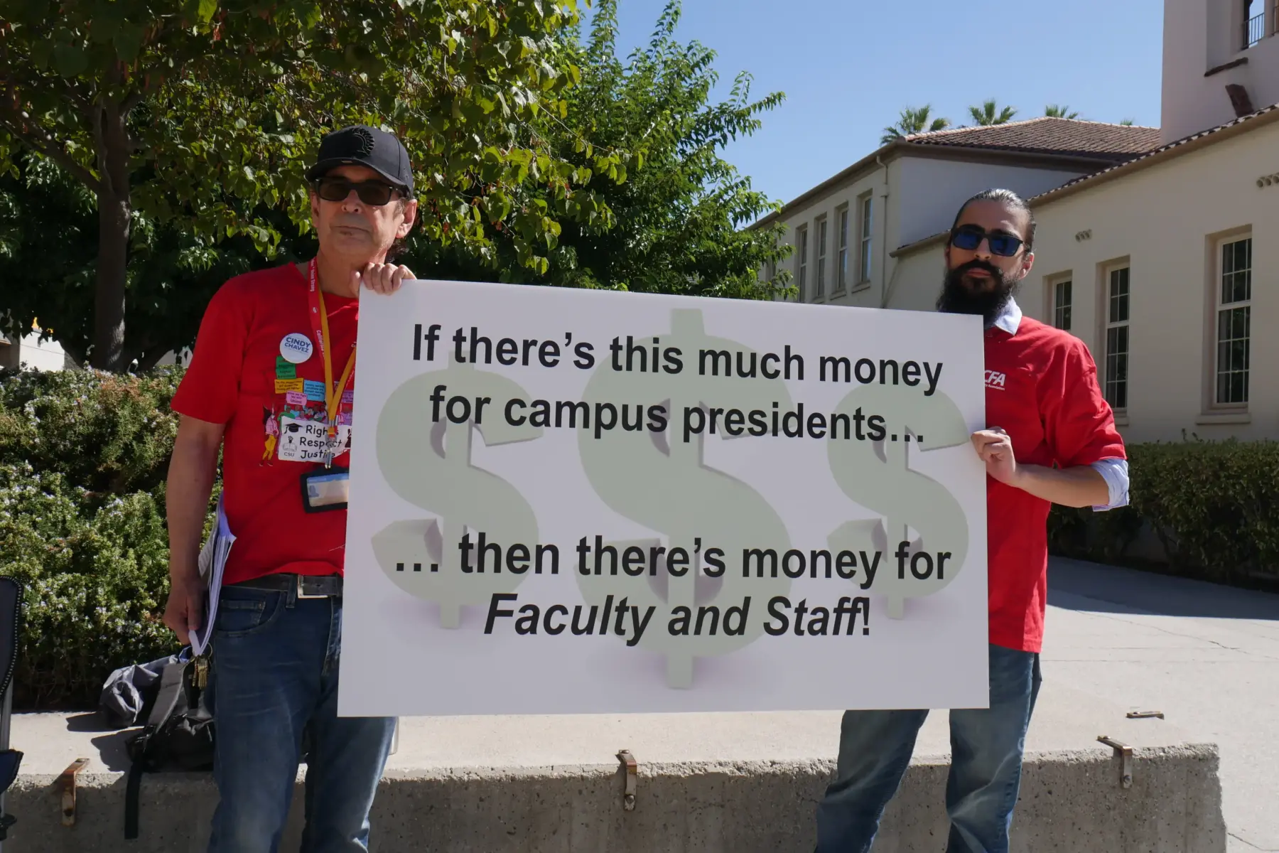 Two people in red CFA t-shirts holding up a sign that says " If there is this much money for campus presidents...then there's money for the Faculty and Staff"