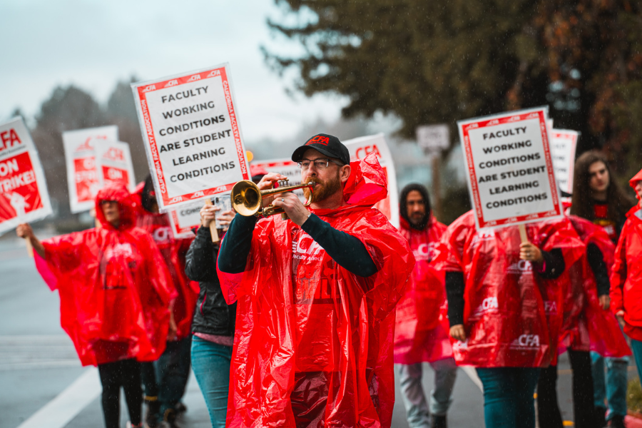 A group of people rallying outside and a person playing the trumpet.