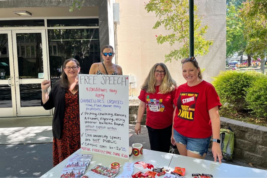 Four people standing by a table outdoors with signs.