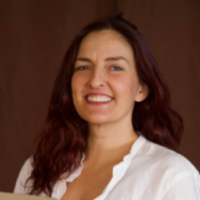 A woman in a white shirt holding a laptop, smiles for a portrait