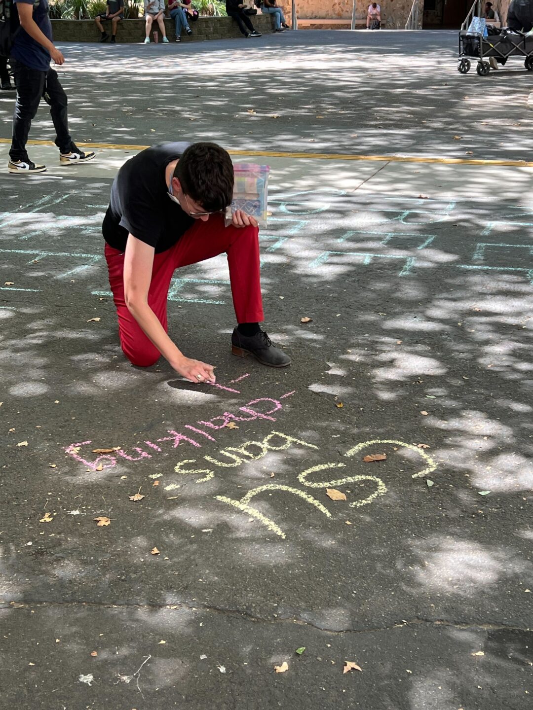 A person writing on the pavement at the CSU Sacramento State campus in chalk "CSU bans Chalking