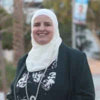 A woman in a black shirt and blazer with a white hijab smile for a photo