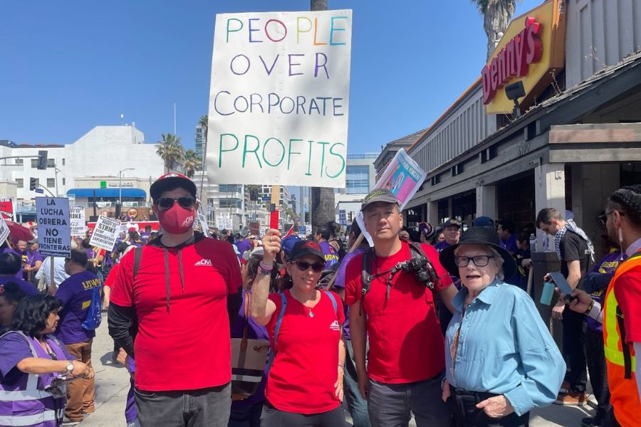  A group od people in red CFA shirts outside a rally with a sign reading " People Over Corporate Profits"