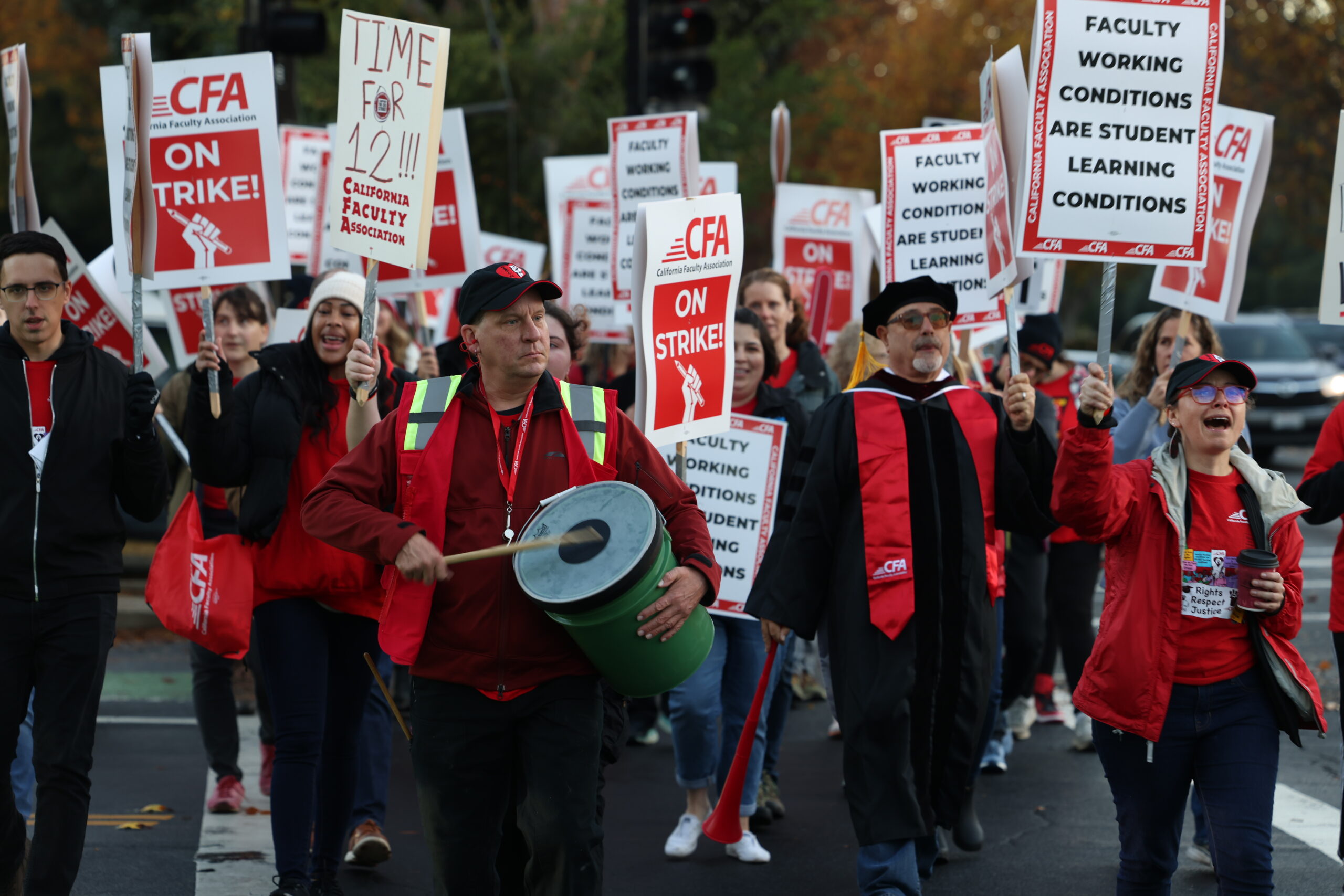 A group of faculty walk the strike line carrying photos and one beats a drum.