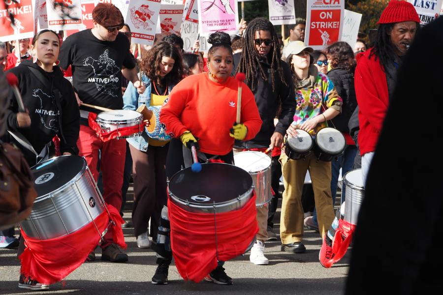 A group of people with drums and signs rallying outdoors.