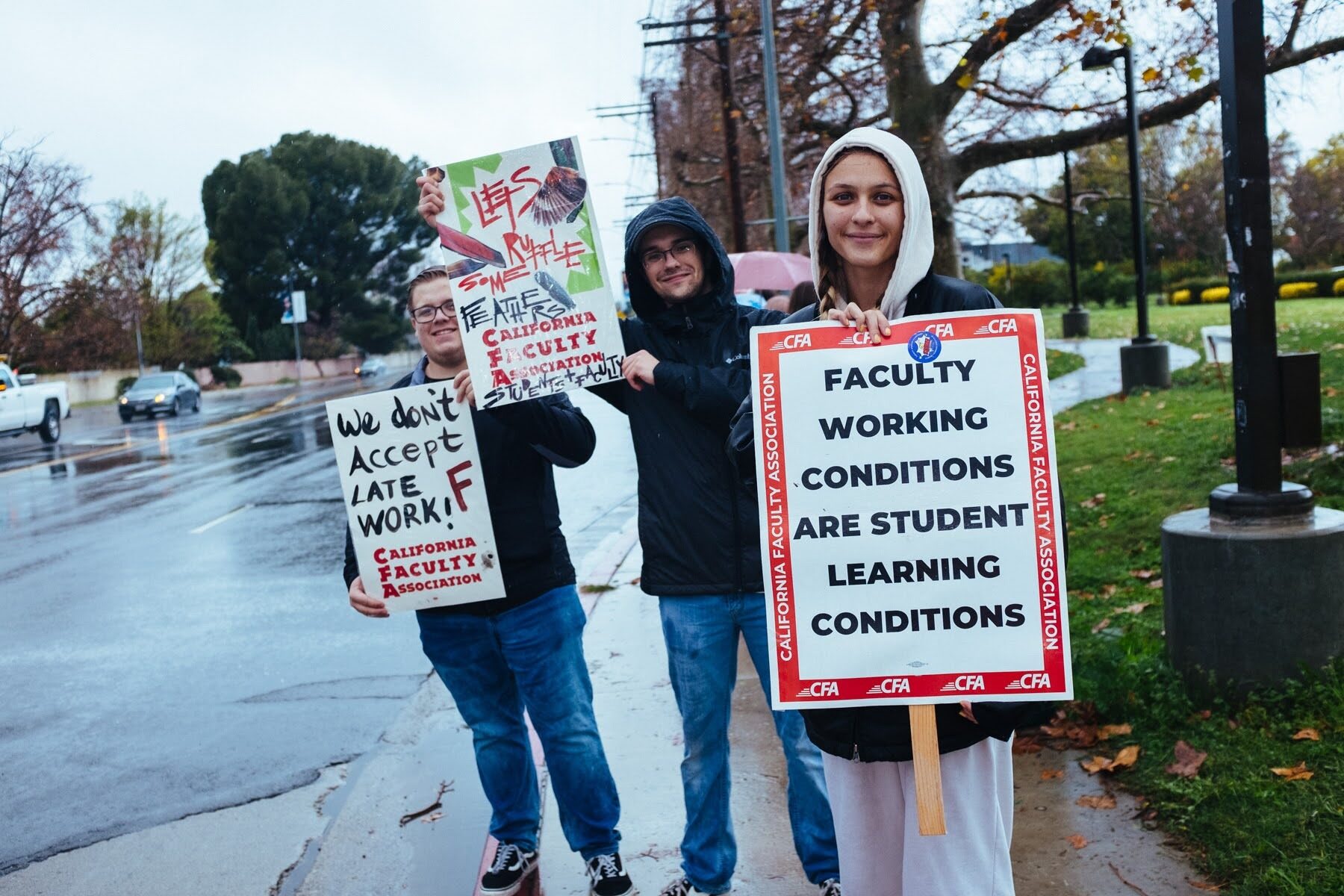 Three students stning outside with signs showing solidarity for CFA