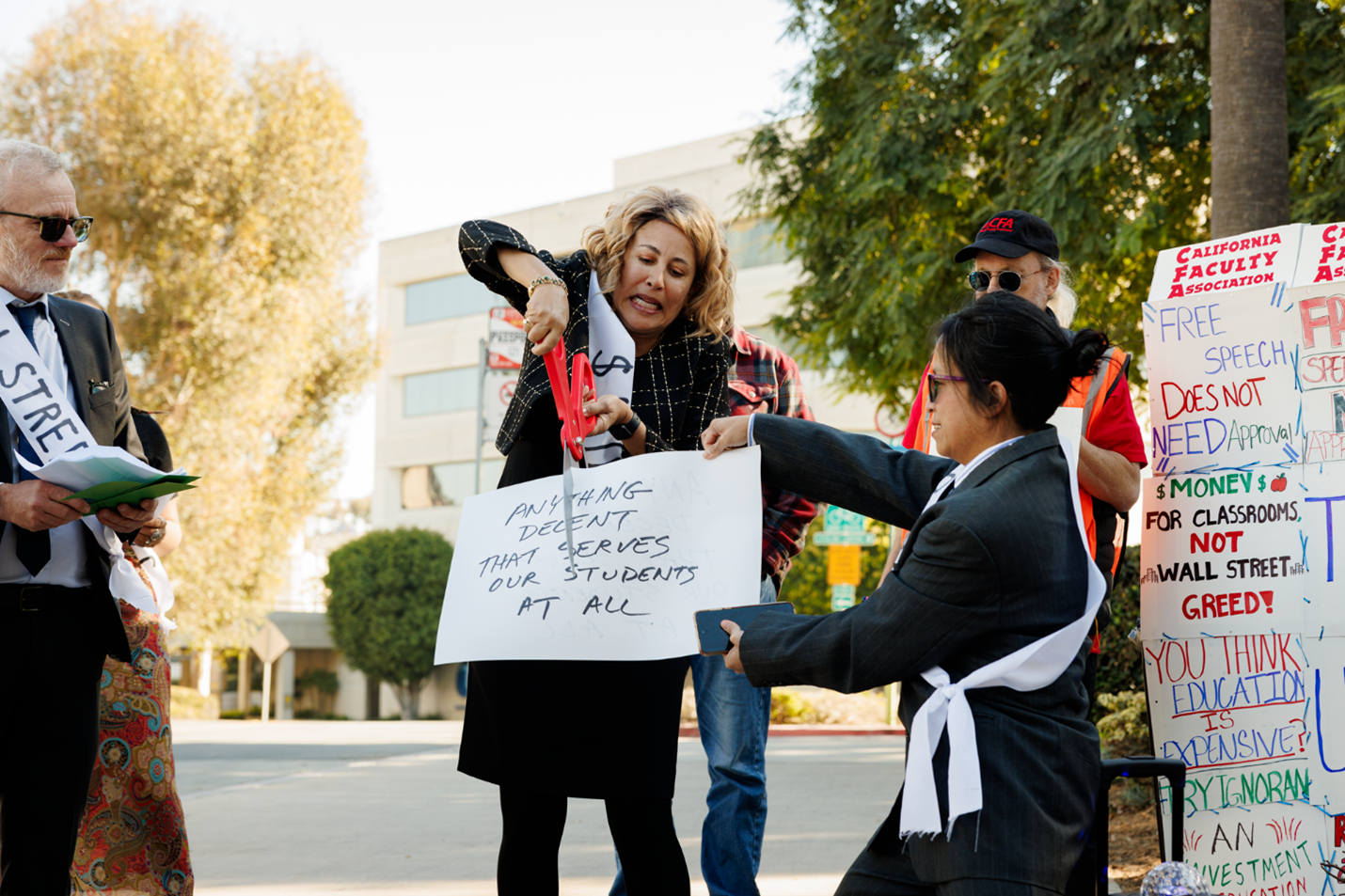 A woman dressed as Chancellor Garcia pretends to cuts a sign and getures her lack of regard for student welfare.