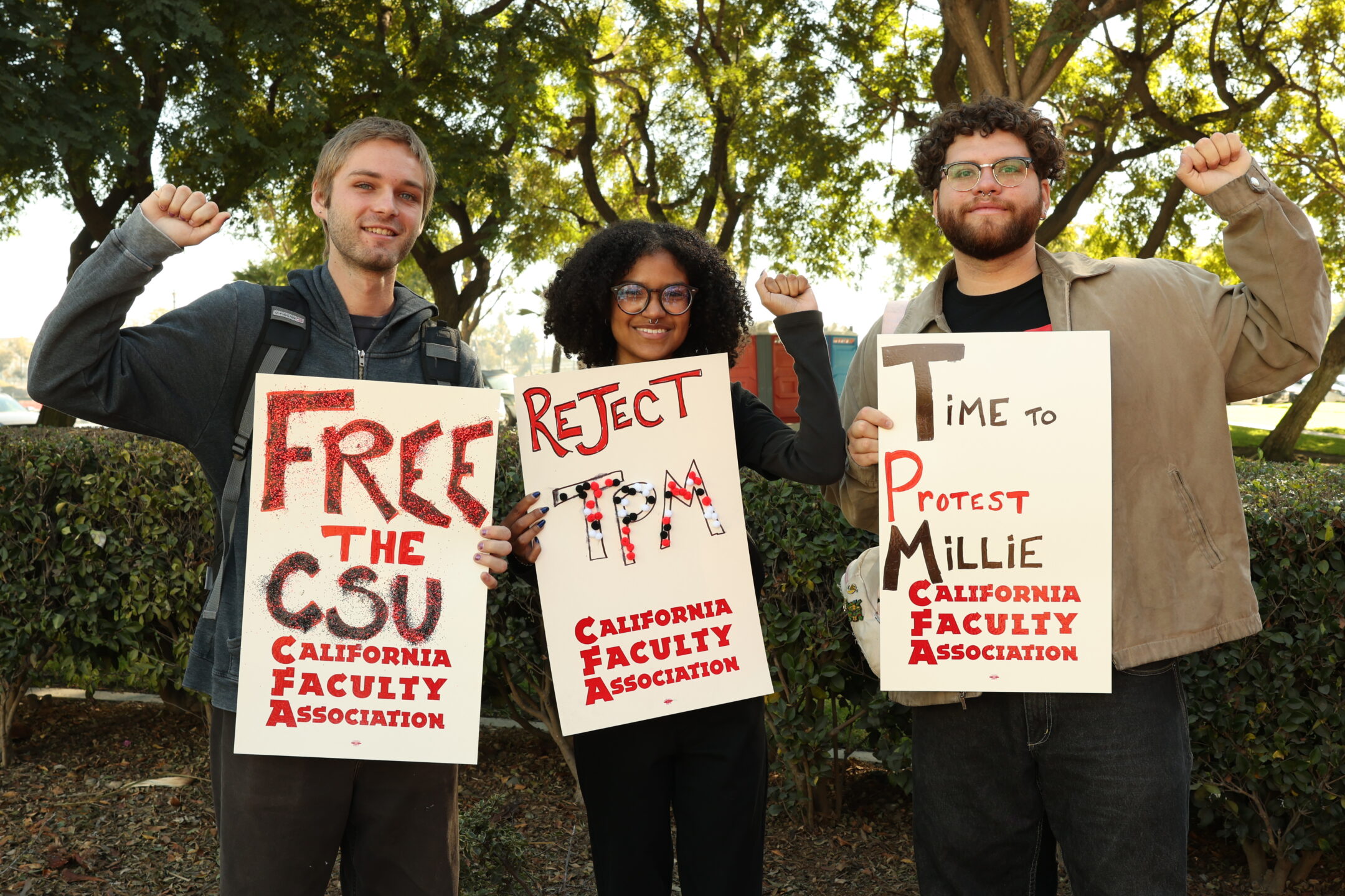 Photo of Three CFA organizers holding picket signs oudoors with raised fists in solidarity against the Time, Place and Manner policy.