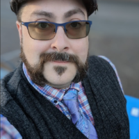 A selfie taken from an above angle. The person is wearing a Jaxon hat, glasses, a vest with a tie and a plaid button up under.